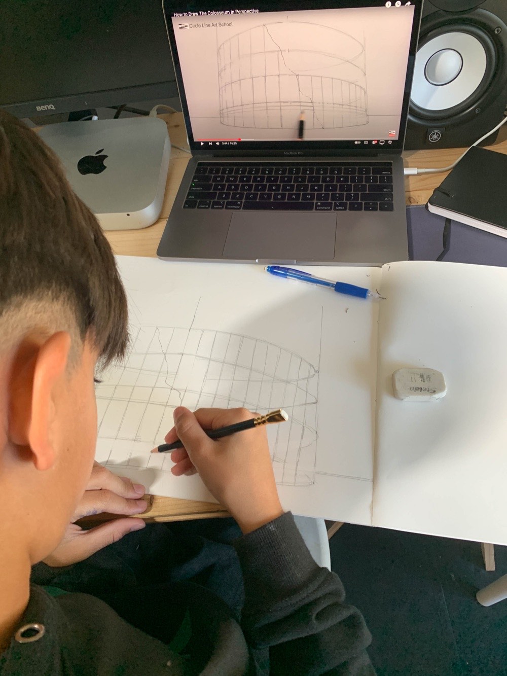 A child sketching a design while following a reference on a laptop